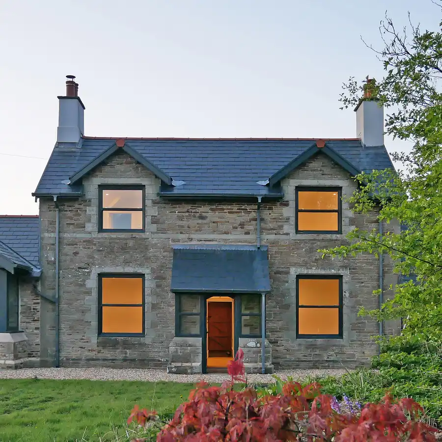 Front elevation of a farmhouse, interior lit at dusk